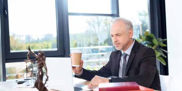 mature lawyer with disposable cup of coffee working with laptop